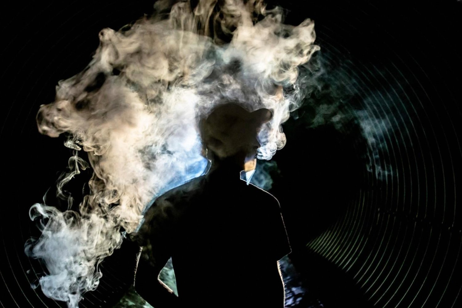 Silhouette of a vaper exhaling a large cloud from a pod system against a dark background